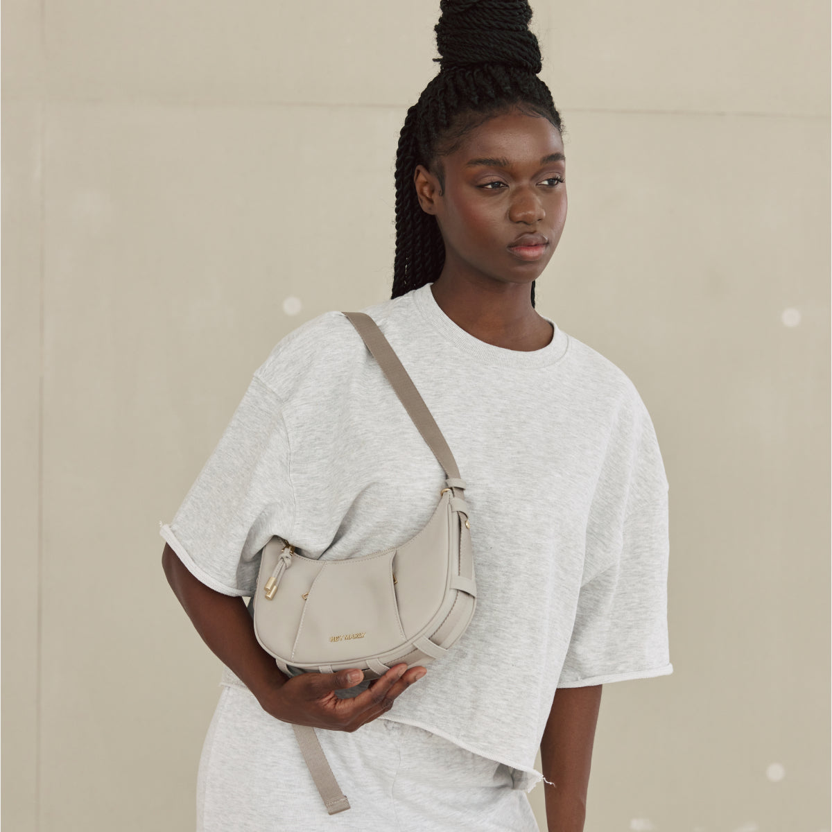 Model vor neutralem Hintergrund mit cremefarbener Tasche über der Schulter