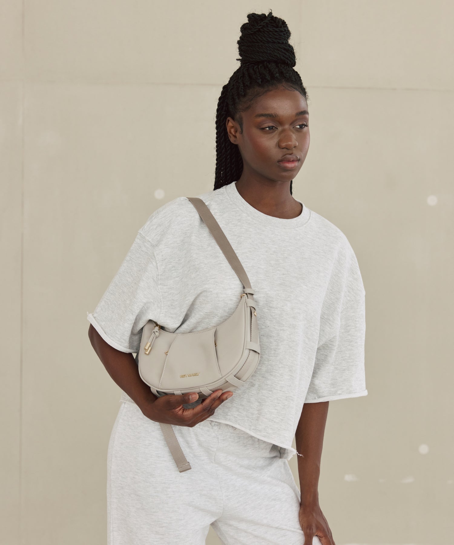 Model vor neutralem Hintergrund mit cremefarbener Tasche über der Schulter